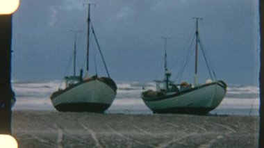 Kıyı yelkenlileri limanda huzur içinde dinleniyor. Hafif okyanus dalgaları bulutlu gökyüzünün altında kıyıya vuruyor.