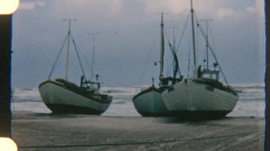 Kumlu sahilde dinlenen tekneler, bulutlu gökyüzünün altında kıyıya vuran dalgalar, sakin ama dramatik bir kıyı sahnesi yaratır.