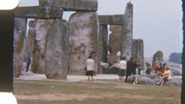 Stonehenge 'in eski tarz görüntüleri, yolda yürüyen turistler, ikonik antik taşları ve manzarayı yakalıyorlar.