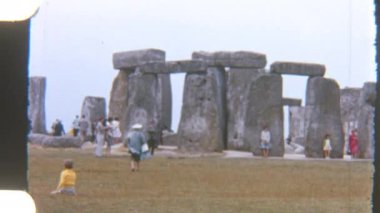 Turistlerin sakin ve bulutlu bir gökyüzü altında sakin bir alanla çevrili görkemli Stonehenge taşlarını keşfettikleri klasik tarzda görüntüler.