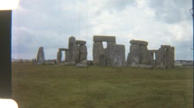 Tarihsel Stonehenge taşları engin alanların üzerinde yükseliyor, dramatik bulutlarla dolu gökyüzüne karşı dizilmiş, antik bir gizemi çağrıştırıyor.