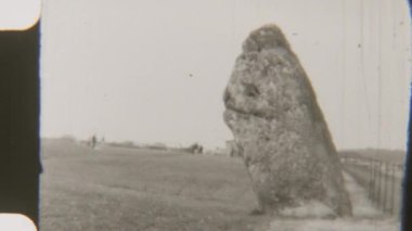 Yalnız bir sarsen taşının siyah ve beyaz görüntüsü. Uzun duruyor, dramatik bir gökyüzüne karşı eski ihtişamını sergiliyor.