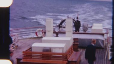 Geminin güvertesinde dinlenen yolcular, açık gökyüzünün altında sakin okyanus manzarasının keyfini çıkarırken, 8 mm 'lik bir filme çekiliyor.