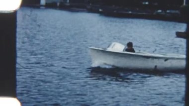 Kaygısız bir çocuk, sakin ve sakin sularda, gölde huzurlu bir günün tadını çıkararak, 8 mm 'lik bir filme çekilen bir tekneyi güvenli bir şekilde sürüyor.
