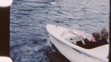 Bir aile sakin bir gölde huzurlu bir tekne yolculuğunun keyfini çıkarıyor. Arka planda görkemli dağlar, 8 mm 'lik bir filme çekiliyor.