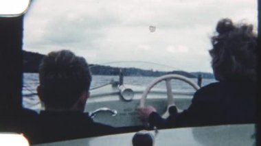 Bir anne ve oğul sakin sularda sakin bir tekne yolculuğunun keyfini çıkarıyorlar, arka planda nefes kesici dağ manzarası, 8 mm 'lik bir filme çekiliyor.