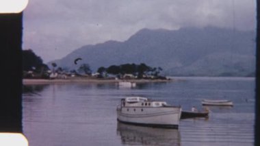 8mm 'lik bir kürekçinin sakin sularda süzülürken sakin bir göl kıyısındaki kanoyla kenetlenmiş bir tekne arasında süzülürken görüntüsü.