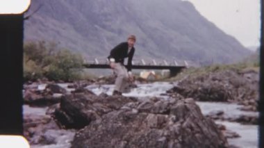 Bir kayadan diğerine atlayarak dereyi dikkatlice geçen bir çocuğun 8 mm 'lik görüntüsü. Gözü, altındaki dereyi dolaşırken bir sonraki taşa odaklanmış.