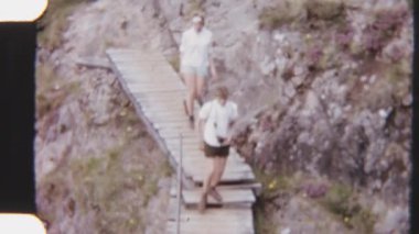 8 mm 'lik kaşiflerin engebeli bir dağ yolunda, dramatik manzaralarla çevrili ahşap bir köprüden geçişlerini gösteren görüntüler.