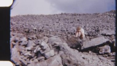 8 mm 'lik bir kadın yürüyüşçünün kayalık arazide oturduğu, mola verdiği ve sakin bir açık havada güneşten korunduğu görüntüler.