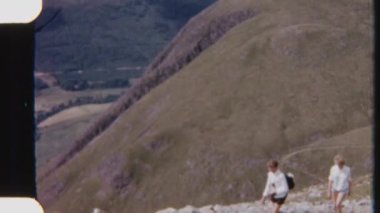 Yürüyüşçülerin engebeli bir dağ yolunda, nefes kesen Highland manzarasıyla gezindiği 8 mm 'lik bir görüntü.