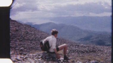 8 mm 'lik bir çocuk kayanın üzerinde oturmuş, kıvrımlı bir nehri dikkatle seyrediyor manzaralı Highlands' da akıyor.