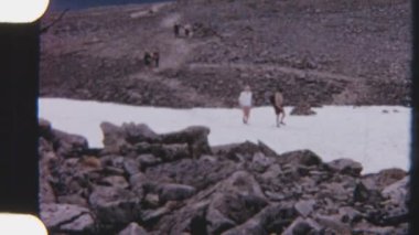8 mm 'lik bir fotoğraf, karlı zeminde yürüyen bir baba ve kız, engebeli kayalar ve sakin bir manzarayla çevrili.