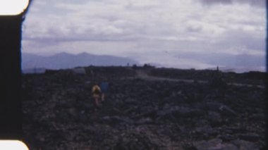 Kaşifler engebeli kayalık bir arazide, sisli dağlık manzaralı, 8mm 'lik klasik bir filme çekilen gezintiler yapıyorlar.
