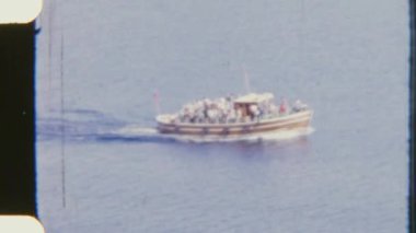 8mm 'lik görüntüler, gezginlerin gün ışığında sakin sularda süzülerek bir teknede sakin bir yolculuk yapmalarını gösteriyor.