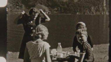 Bir aile göl kenarında pikniğin tadını çıkarıyor. Etrafı yemyeşil ve sakin doğa ile çevrili. Nostaljik 8 mm filmle çekilmiş.
