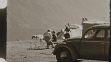 Bir aile gölün kenarında manzaralı dağ manzaralı kamp yapmayı seviyor, ön planda eski model bir Volkswagen Beetle, nostaljik 8 mm 'lik bir filmde yer alıyor.