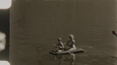 Kardeşler, 8 mm 'lik nostaljik bir gölde çekilen şişme bir teknede kürek çekerken eğlenirler.