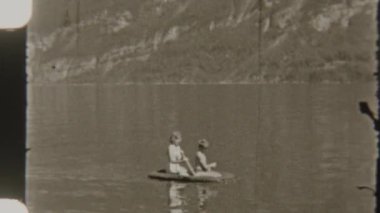 Kardeşler, 8 mm 'lik nostaljik bir filmde çekilen, şişme bir teknede, sakin bir gölde kürek çekerler.