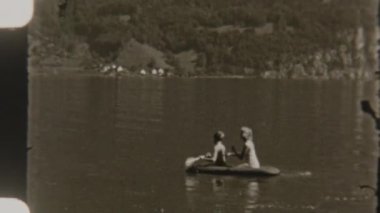 Şen şakrak kardeşler, 8 mm 'lik nostaljik bir filmde çekilen şişme bir tekneyle sessiz bir gölde kürek çekerler.