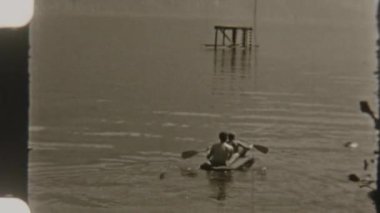 Bir baba ve oğlu sessiz bir gölde birlikte kürek çekiyorlar şişme bir teknede, nostaljik bir 8 mm filmle çekiliyor.