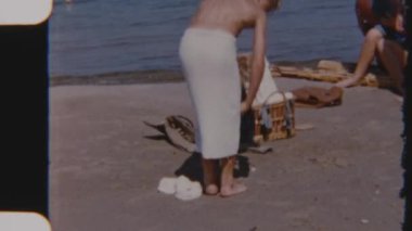 Klasik bir 8 mm 'lik film, bir çocuğu sahilde mayolarını değiştirerek yüzmeye hazırlanırken yakalar. Arka planda okyanus dalgaları yavaşça dalgalanır.