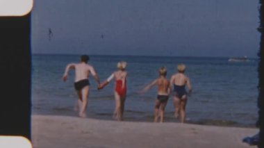 Bir aile, sakin sulara dalmadan önce, çıplak ayakla ve kaygısızca, günışığı kıyılarında el ele yarışır, hepsi de 8 mm 'lik filmlerde yakalanır.