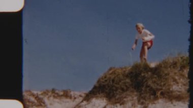 8mm 'lik bir film, aile üyelerini açık mavi gökyüzünün altında çimenli bir kumuldan neşeyle atlarken yakalıyor. Açık havada bir eğlence ve kahkaha anı yaratıyor.