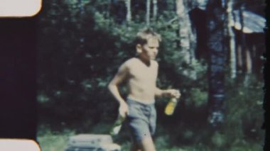 Klasik bir 8 mm 'lik film, yemek gündüz vakti hazırlanırken elinde şişeler dolusu içecekle aile kampına doğru yürüyen bir çocuğu yakalar.