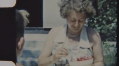 Bir anne sıcak, güneşli bir ortamda sıcak bir kaseden yemek servisi yapar, neşeli ve sade bir atmosfer yaratır, 8mm 'lik bir filme çekilir.