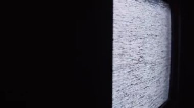 Eski bir CRT televizyon ekranının yakın çekim görüntüsü statik gürültüyü gösteriyor, rastgele parazitlenme ve kumlu bir doku ile titreşiyor, nostaljik, klasik bir atmosfer yaratıyor.