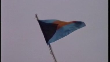 Yakın çekim, açık hava tersanesinde soluk, bulutlu bir gökyüzüne karşı rüzgarda dalgalanan kendine özgü mavi, siyah ve kırmızı üç renkli bir tasarıma sahip bir bayrağı yakalar.