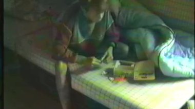 Analog bir video, genç bir çocuğun bir yatakta oturup önündeki oyuncağı incelediğini gösteriyor. Görüntülerin kalitesi ise eski video çekiciliğini ön plana çıkarıyor.