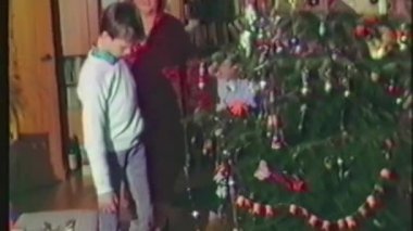 Eski bir ev videosundan bir sahne, güzel dekore edilmiş bir Noel ağacının etrafında yürürken bir ailenin el ele tutuşup tatil sezonunda çok değerli bir anı yakaladığını gösteriyor.