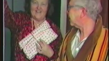 Eski bir ev videosunda, Noel 'i birlikte kutlarken gülümseyen yaşlı bir çift görülüyor. Kırmızı elbiseli kadın elinde bir hediye, gözlüklü adam ve kahverengi bornoz giyiyor.