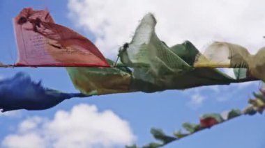 Himalaya rüzgarında dalgalanan renkli dua bayrakları, mavi gökyüzüne karşı.