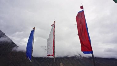 Tibet bayrakları rüzgarda dalgalanıyor dramatik bulutlu gökyüzüne karşı, Nepal 'in görkemli sıradağları nefes kesen bir zemin oluşturuyor, Himalayaların ruhani ve doğal güzelliklerini yakalıyor.