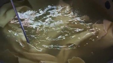 Sarı kumaş temizleme işleminin bir parçası olarak bir kabın içinde yavaşça karıştırılır ve yaklaşan boyama işlemine hazırlanır.