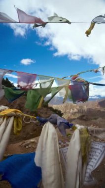 Rüzgarda dalgalanan canlı dua bayrakları, Nepal 'in görkemli dağ zirvelerinin zeminine kurulmuş, sakin ve renkli bir sahne yaratıyor.