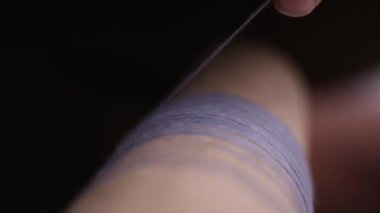 Örgü örmek veya dokumak için iplik diziliminin detaylı sürecini gösteren ipliğin dikkatlice bir makaraya bağlandığı yakın plan görüntüsü.
