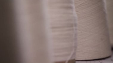 Bir sıra beyaz iplik makarasının dinamik raf odak görüntüsü, odağı en uzaktaki makaradan kameraya en yakın olana kaydırmak, pürüzsüz bir bulanıklık etkisi yaratır