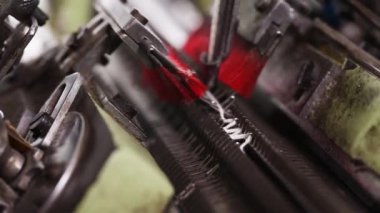 Beyaz iplik dikkatlice örgü makinesine bağlanıyor. İğneler, sürecin hassasiyetini gösteriyor.