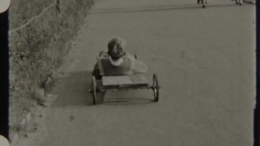 8 mm 'lik bir filmde çekilen genç bir çocuk, bir sabun kutusu arabasıyla manzaralı bir kırsal yolda süzülerek, yemyeşil ağaçların nostaljik arka planında hız kazanıyor.