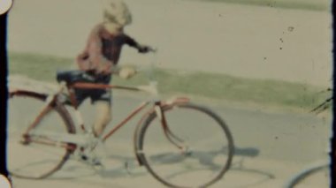 Neşeli bir çocuk güneşli bir günde sakin bir banliyö sokağında bisikletini pedallar.