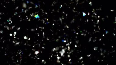 Büyüleyici, yavaş çekim rüya gibi gümüş konfetilerin zarif bir şekilde yükselişi, yukarı doğru siyah bir arka plana doğru süzülürken ışıldaması.