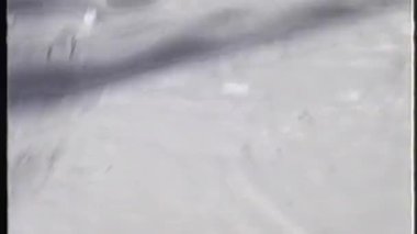 Kumlu bir analog video kayakçı perspektifinden kayağın kenarları ve tabanı bulanık, odak dışı bir arkaplan karşısında görüntülenir.