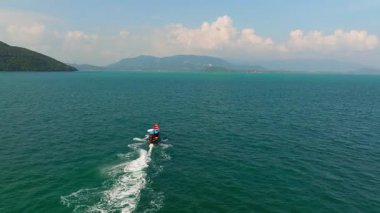 Geleneksel bir uzun kuyruklu tekne, yemyeşil adalarla çevrili canlı mavi sularda süzülerek Tayland 'ın tropikal deniz manzarasının güzelliğini yakalar.