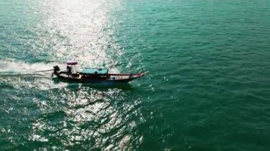 Çarpıcı bir yay görüntüsü, Tayland 'ın turkuaz denizlerini incelikle keşfeden uzun kuyruklu bir tekneyi yakalar ve el değmemiş sularının ve tropik cazibesinin güzelliğini gözler önüne serer.