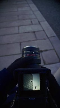 Elinde klasik bir kamera olan bir sokak fotoğrafçısı şehir mimarisinin görüntülerini çeker, şehir binalarını klasik bir estetik filmle çerçeveler.