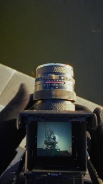 Bir fotoğrafçı, mavi gökyüzüne karşı klasik bir film kamerasının görüş açısı üzerinden yüksek bir ağ yapısını çerçeveler.